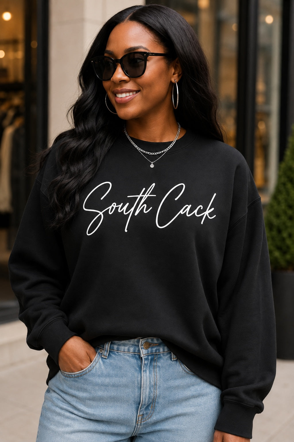 Woman wearing a black saysomethingteez crewneck sweatshirt with white South Cack script text, paired with blue jeans.