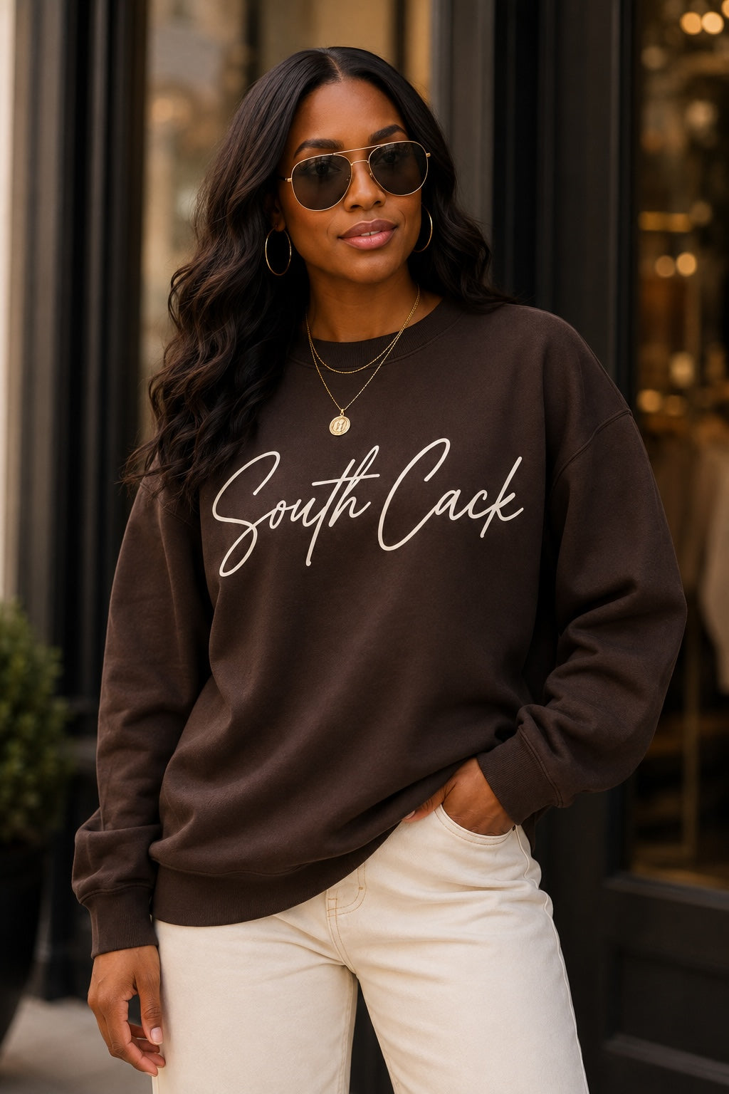 Model wearing a saysomethingteez dark brown crewneck sweatshirt with white South Cack script graphic and sunglasses.