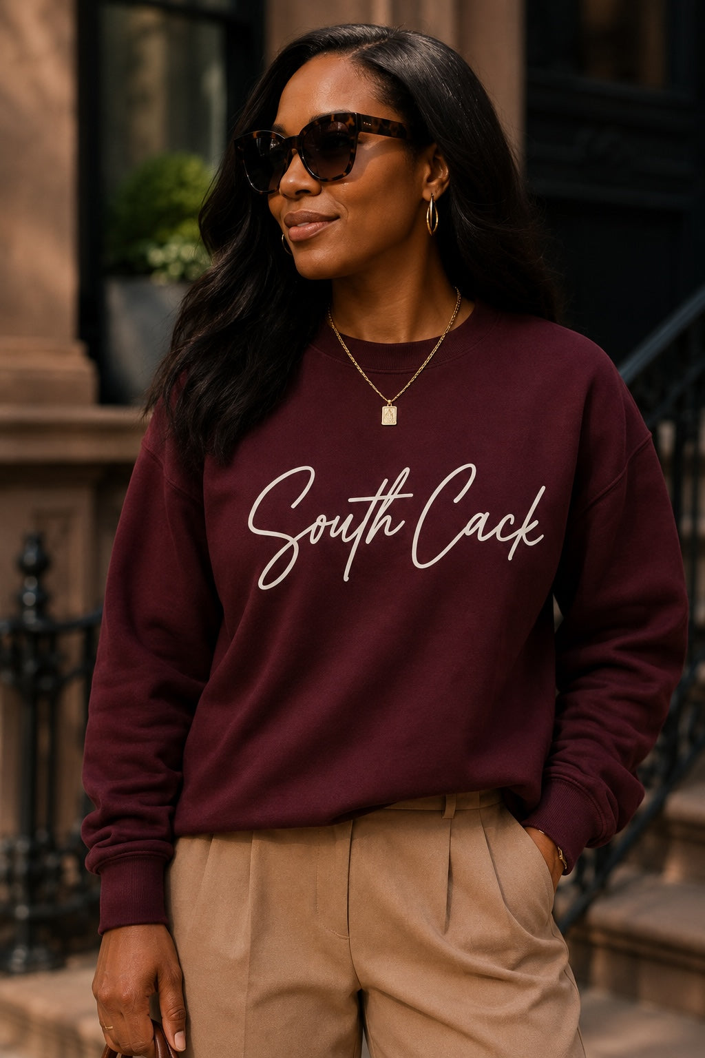 Woman wearing a saysomethingteez maroon crewneck sweatshirt with white South Cack script graphic and tan trousers.